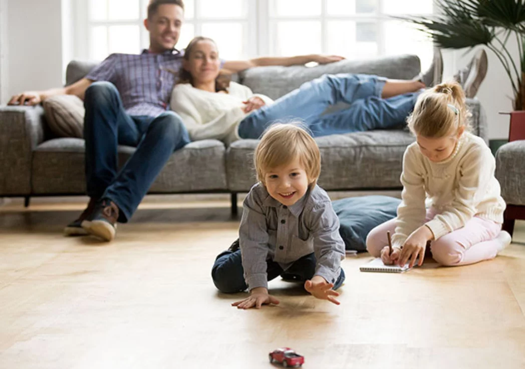 Une famille se détend dans le salon pendant que leurs enfants jouent par terre, profitant du temps ensemble.