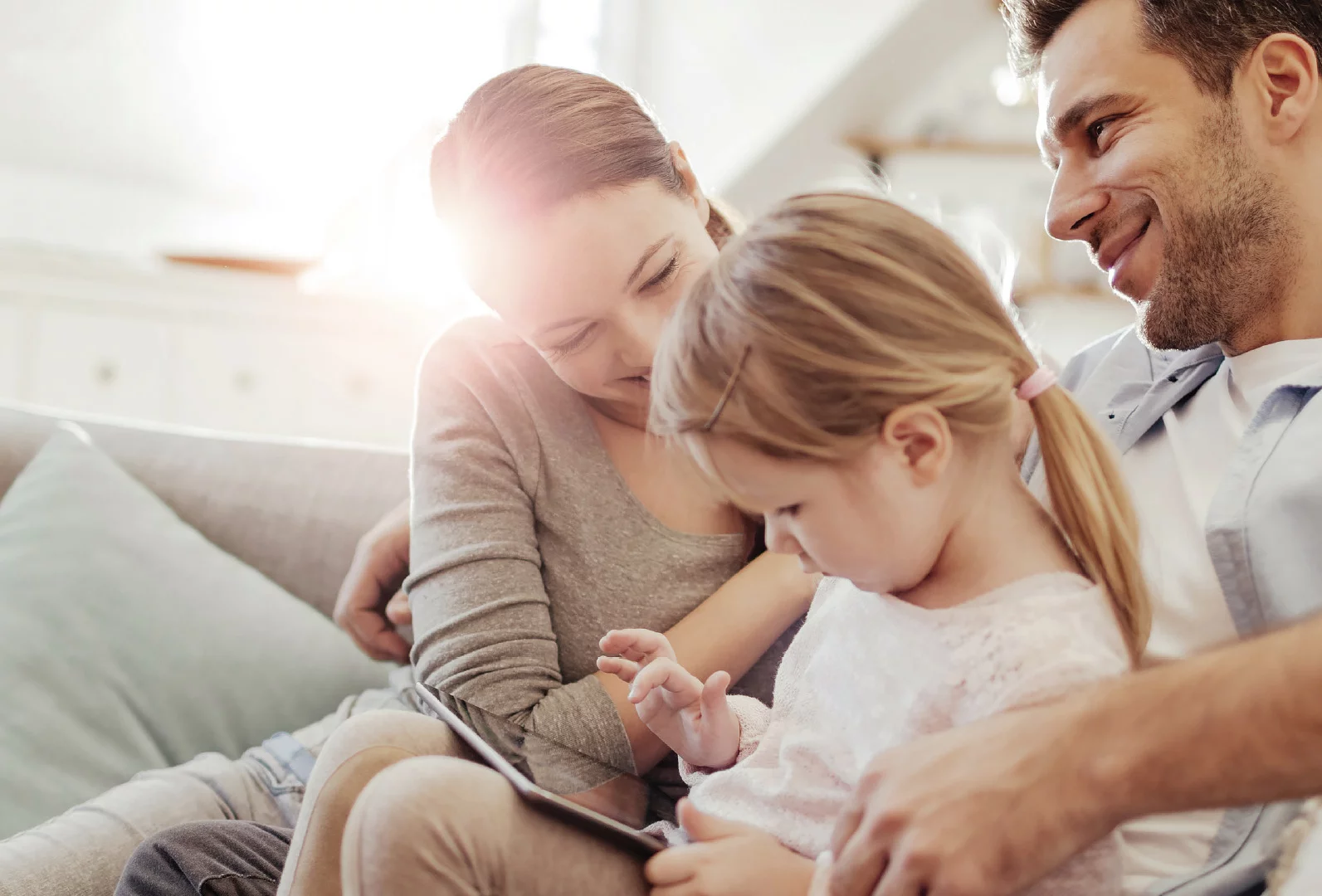 Une famille heureuse profitant de temps ensemble à la maison, une petite fille utilisant une tablette sur le canapé.