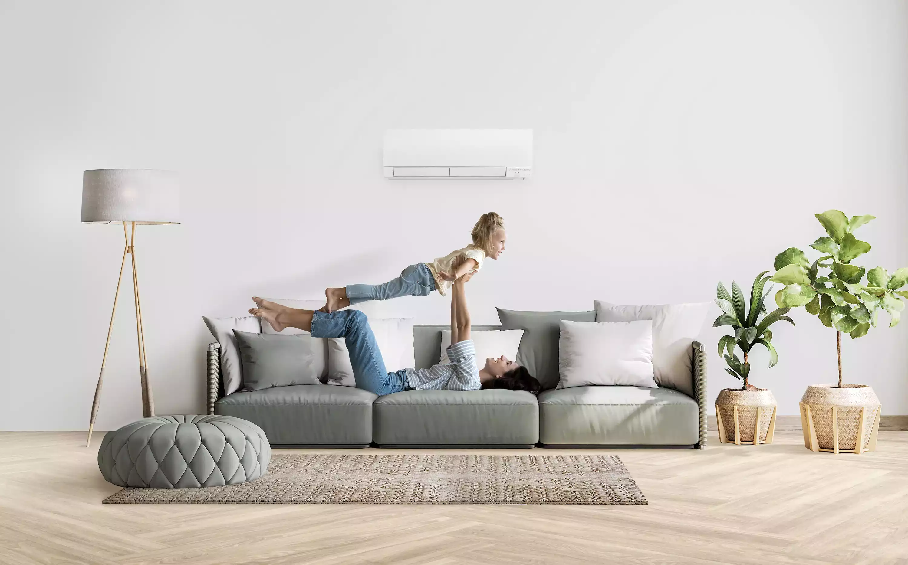 Enfant volant joyeusement au-dessus d'une femme allongée sur un canapé, tous deux sous un climatiseur mural haute efficacité dans un salon bien aménagé.