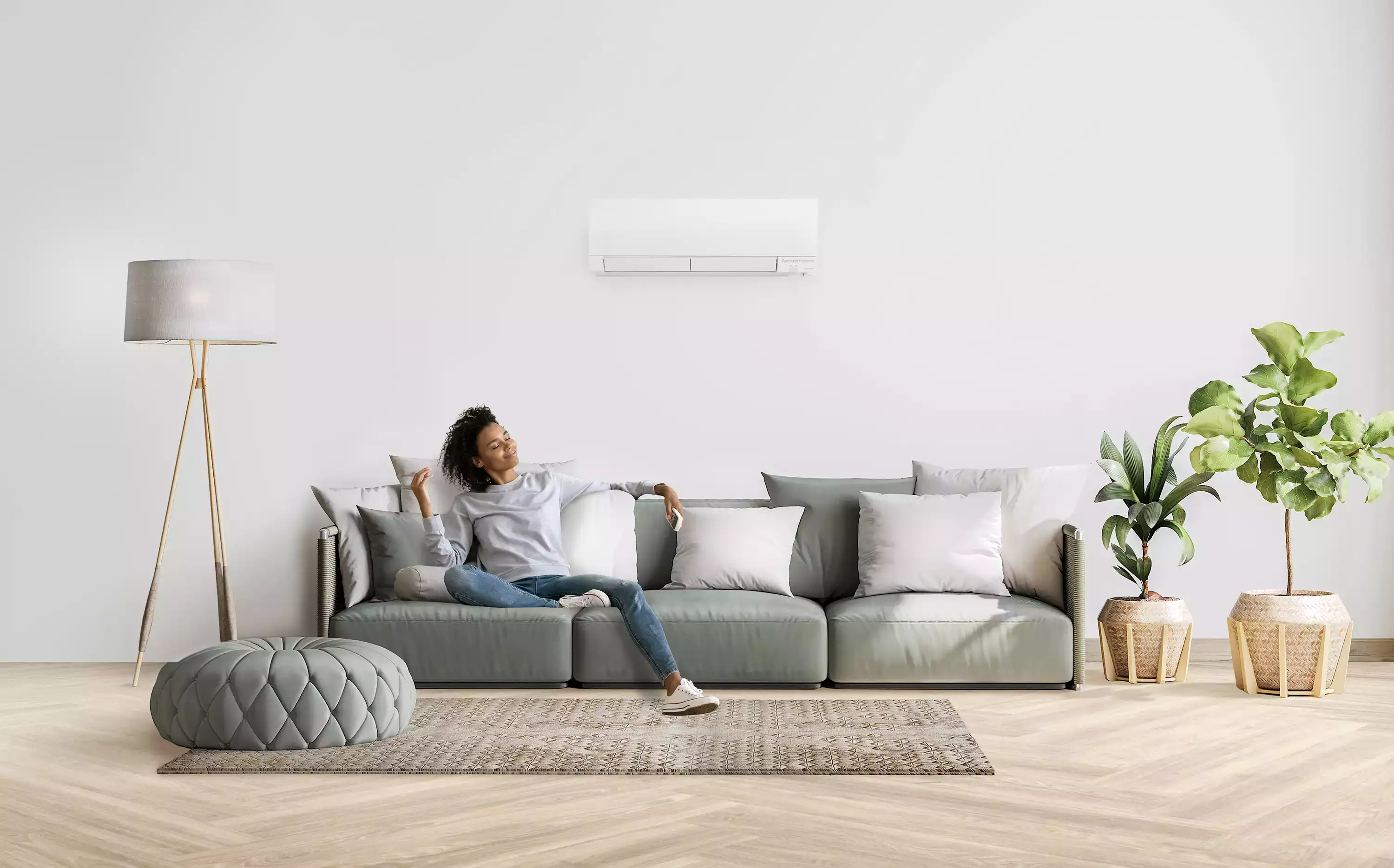 Femme se relaxant sur un canapé, tenant une télécommande, sous un climatiseur mural dans un salon lumineux.